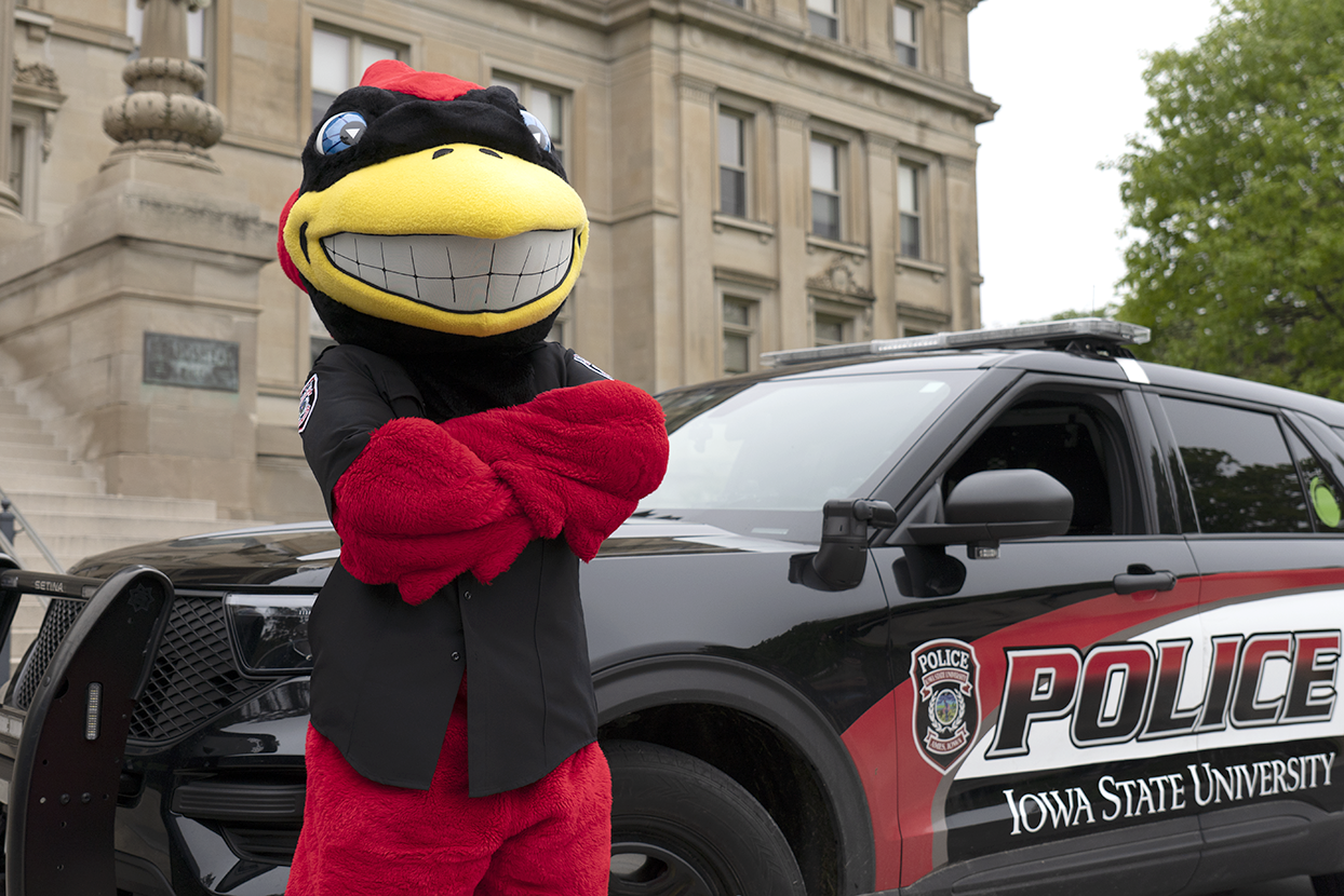 Cy mascot poses with an ISU Police car outside Beardshear Hall.