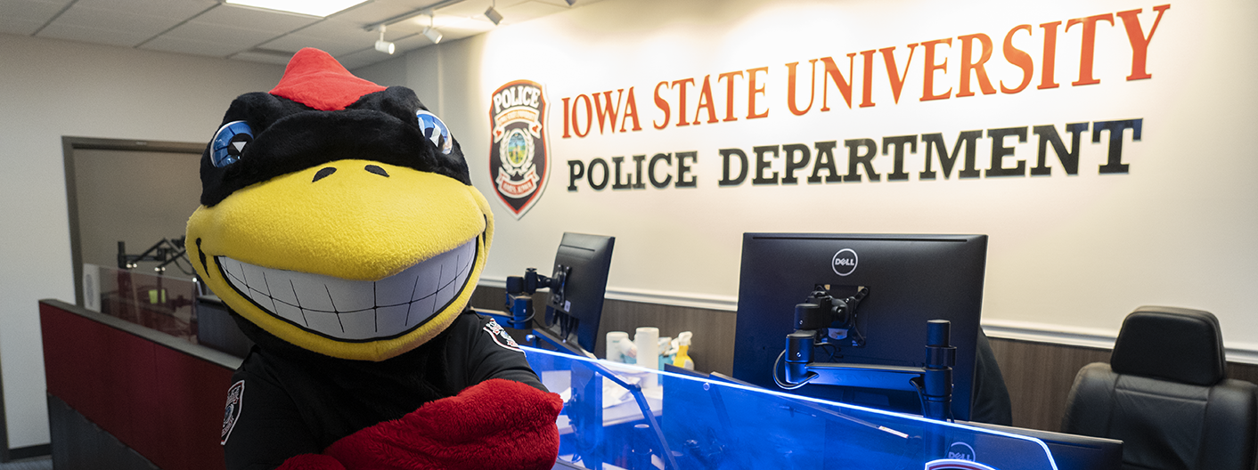 Cy mascot poses in the ISU Police dispatch area.